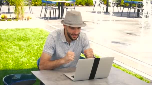 Jocund ανδρικό πρόσωπο που απολαύει επιτυχής στοίχημα στην ιστοσελίδα στοιχημάτων με φορητό υπολογιστή κοντά στο συντριβάνι. - Πλάνα, βίντεο