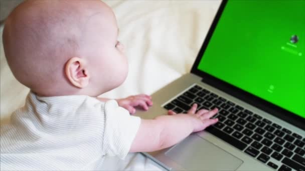 Niño de 6 meses de edad está acostado en la cama delante de la computadora portátil con pantalla de croma clave
 - Imágenes, Vídeo