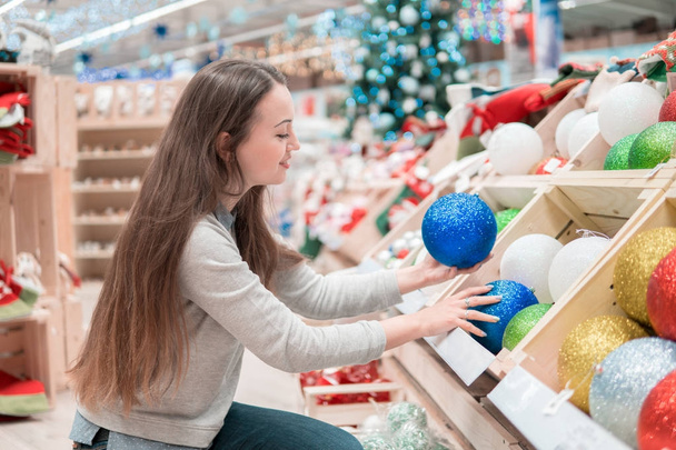 Cheerful happy customer girl choosing Christmas tree decoration balls - Photo, Image