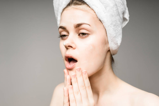 молодая девушка с чистой кожей, с белым полотенцем на голове, нанося крем на лицо
 - Фото, изображение