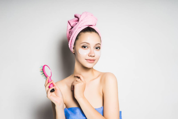 young fresh girl with a pink towel on her head, under the eyes of silicone patches, holds a comb - Fotoğraf, Görsel