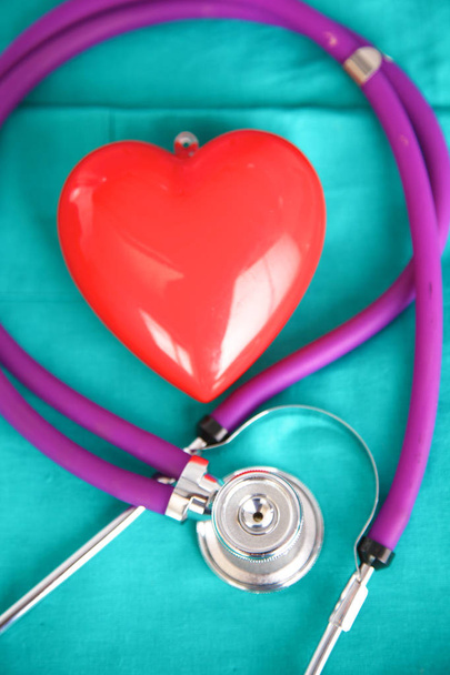 medizinisches Stethoskop in Herzform verdreht liegend auf Krankenakte und blauer Arztuniform Nahaufnahme - Foto, Bild