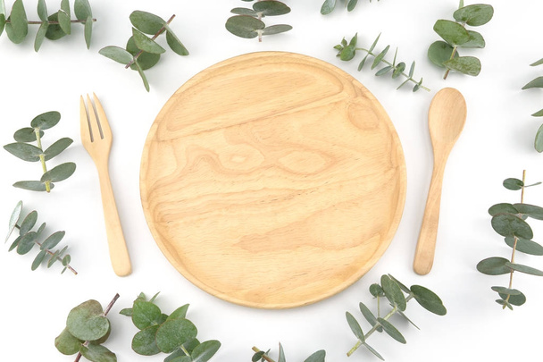 Ξύλινο πιάτο, κουτάλι και πιρούνι διακοσμημένα με φύλλα ευκαλύπτου μωρό  - Φωτογραφία, εικόνα
