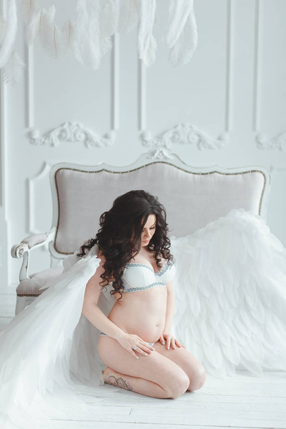 Beautiful young pregnant girl with big angel wings in white studio. - Valokuva, kuva