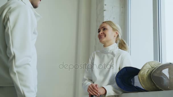 Two young fencers man and woman chatting after fencing tournament indoors - Séquence, vidéo