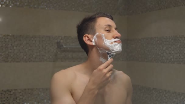 Young man shaves in front of mirror - Footage, Video