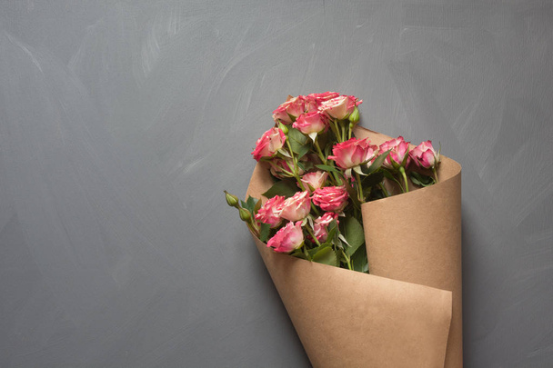 Bouquet of pink bush roses wrapped in craft paper on gray background. Copy space. - 写真・画像