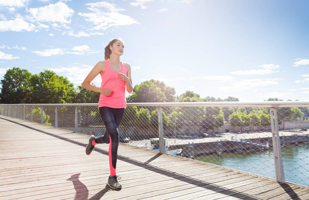 Young active woman in sportswear running across a bridge during morning run - Фото, изображение