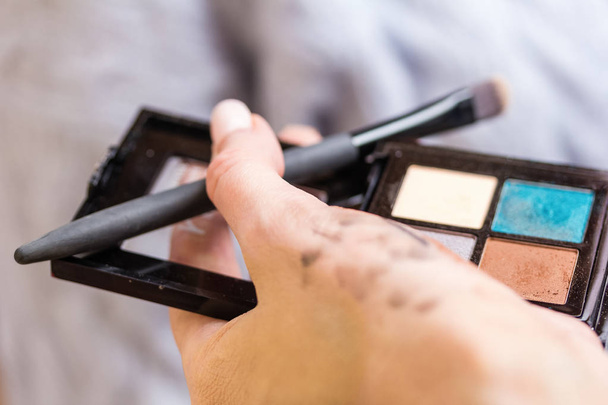 eine Palette von Lidschatten und Make-up-Pinseln in den Händen eines Visagisten mit Spuren von Kosmetiktests - Foto, Bild