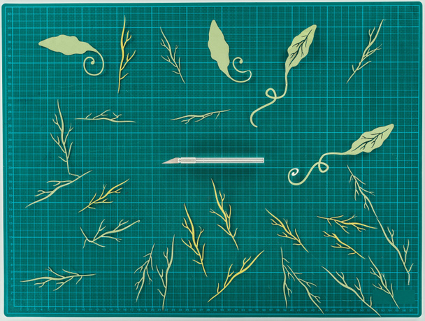 Top view of cut paper leaves and twigs with knife for scrapbooking decoration on turquoise scale - Photo, Image