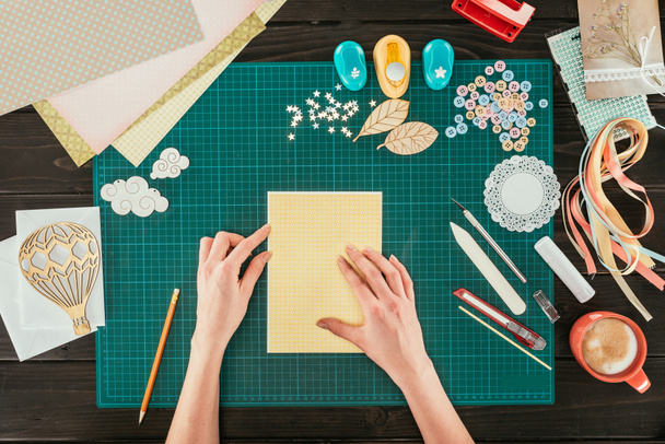 imagen recortada del diseñador sentado en la mesa de trabajo con plantilla para la tarjeta postal scrapbooking
 - Foto, Imagen