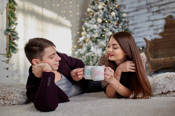 couple holding mugs against  christmas tree in room  - Foto, Imagen