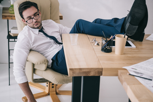 businessman sleeping in armchair with feet on table at office - Foto, Bild