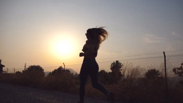 Following to sporty girl jogging in country road at sunrise. Young woman running outdoors at morning. Healthy active lifestyle. Slow motion - Video