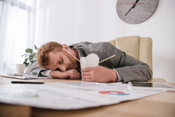 exhausted young businessman sleeping with box of take away noodles at workplace - Photo, Image