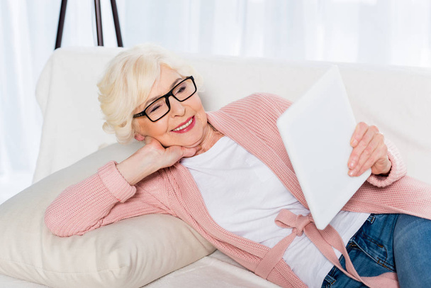 Szemüvegek segítségével tabletta, miközben otthon a kanapén pihen-mosolygó vezető nő portréja - Fotó, kép