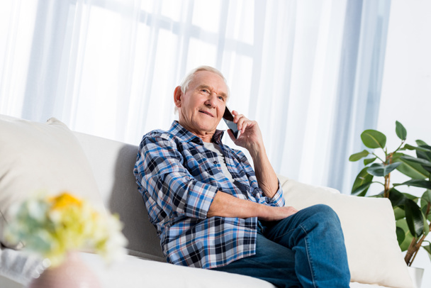 pensive senior man talking on smartphone while sitting on sofa at home - Foto, Imagem