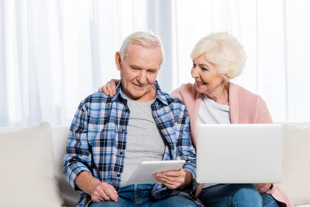 retrato de la sonriente esposa y esposo mayores usando dispositivos digitales en casa
 - Foto, Imagen