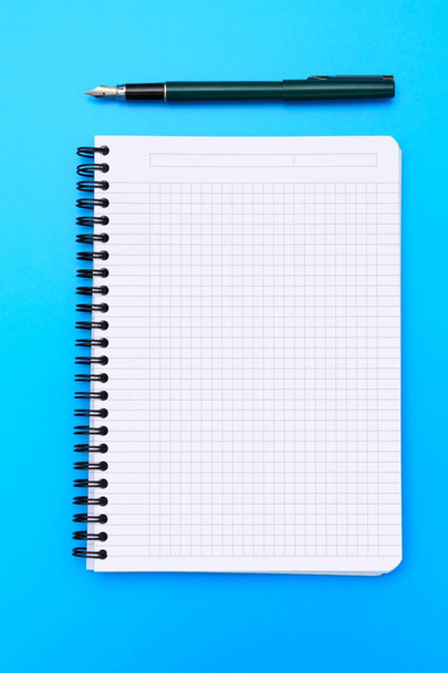 Το Top view για ένα κενό σημειωματάριο με στυλό επίπεδη θέσει σε μπλε φόντο. - Φωτογραφία, εικόνα
