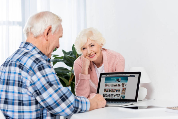 portrait of senior wife looking at husband using laptop at home - Foto, Imagen