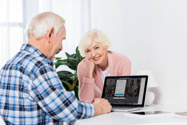 portrait of smiling senior woman looking at husband using laptop at home - Foto, imagen