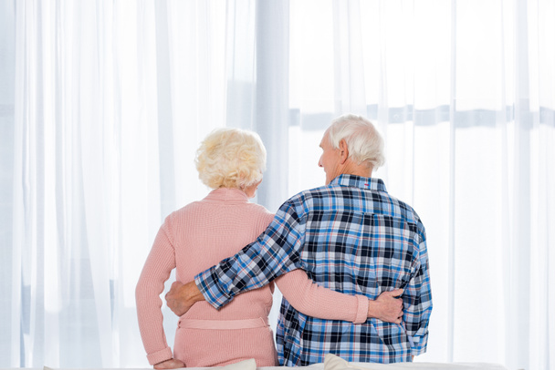beautiful senior couple embracing in front of window - Photo, Image