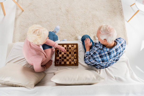 top view of senior couple playing chess at home on couch - Zdjęcie, obraz