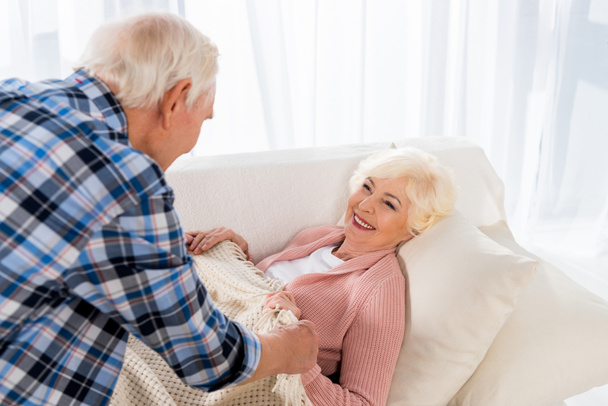 Senior man bedekking gelukkige vrouw met deken op gezellige Bank - Foto, afbeelding
