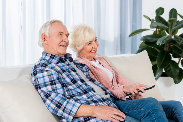 счастливая пожилая пара с пультом дистанционного управления смотреть телевизор на диване
 - Фото, изображение
