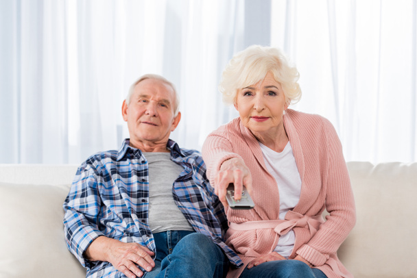senior couple with remote control watching tv on couch - Фото, зображення