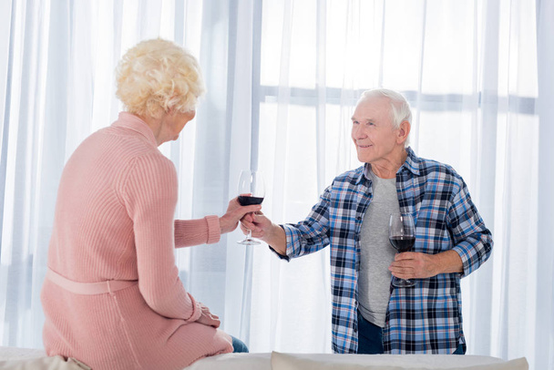 赤ワインのグラスを自宅の妻に与える年配の男性の側面図 - 写真・画像