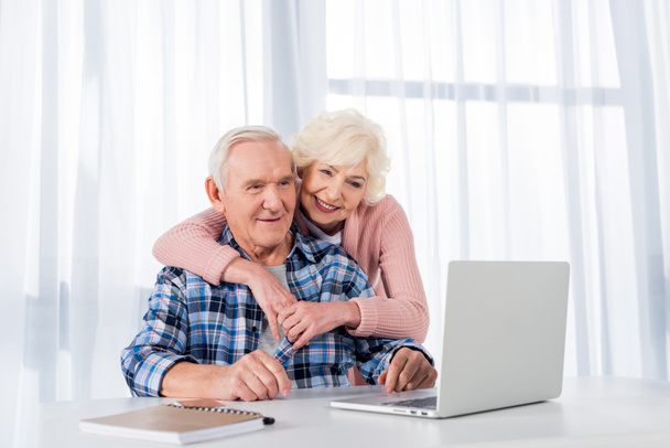 портрет веселой пожилой пары, использующей ноутбук вместе дома
 - Фото, изображение