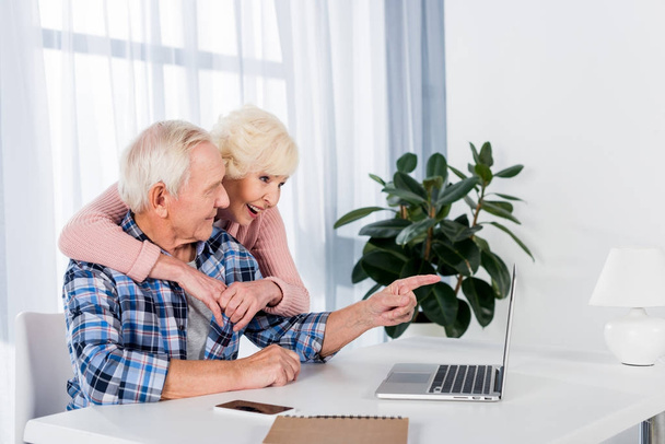 side view of happy senior couple using laptop together at home - Valokuva, kuva