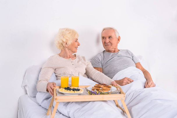 happy senior couple having breakfast in bed together at home - Foto, imagen