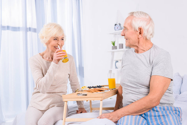happy senior couple having breakfast in bed together at home - 写真・画像