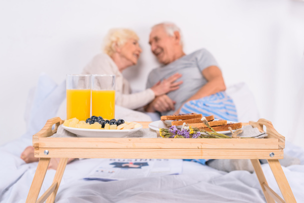 selective focus of breakfast and happy senior couple in bed at home - Foto, immagini