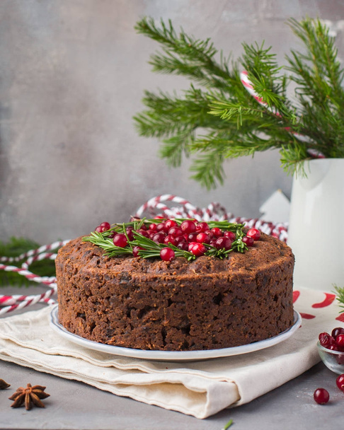 Pudding traditionnel anglais de Noël (gâteau aux fruits) avec romarin et canneberges sur plaque blanche sur un fond clair en béton. Décor de Noël de la table
.   - Photo, image