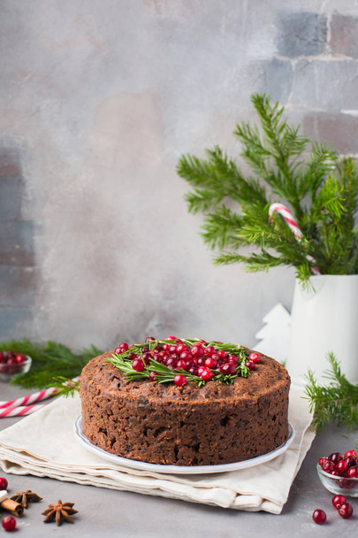 Traditional Christmas English pudding (fruit cake) with rosemary and cranberries on white plate on a concrete light background. Christmas decor of the table.   - Foto, immagini
