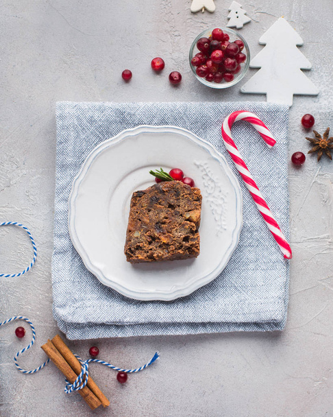 A piece of traditional Christmas English pudding (fruit cake) on white plate on a concrete light background. Christmas decor of the table.  Flat lay, top view - Foto, Bild