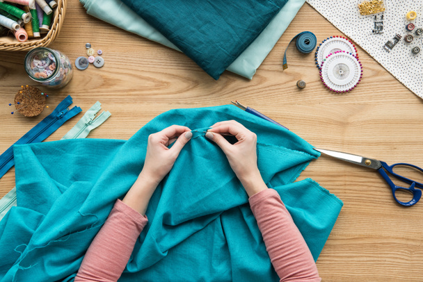 top view of cropped female hands sewing fabric with needle at seamstress workplace - 写真・画像