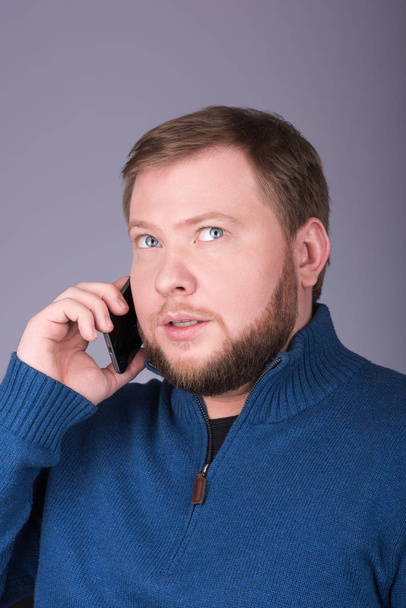 Young man with beard talking on the phone. The gaze is directed upwards - Foto, Imagen
