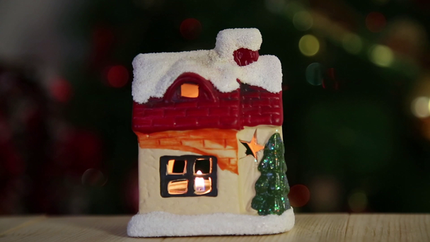 Karácsonyi játék ház egy gyertyát. Tűz a Windows, a háttérben egy karácsonyfa a hóval borított gyönyörű ház - Felvétel, videó