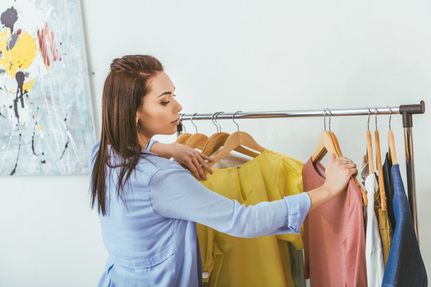 attractive designer looking at shirts on hangers  - Photo, Image