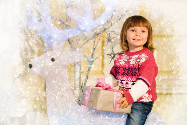 Маленька весела дівчинка з подарунком у руках сідає на оленя
. - Фото, зображення