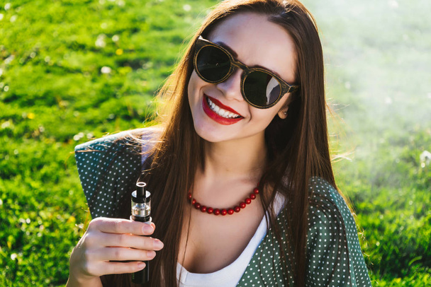 Happy fashion smiling Woman in sunglasses smoking vape on street,smoke - Foto, afbeelding