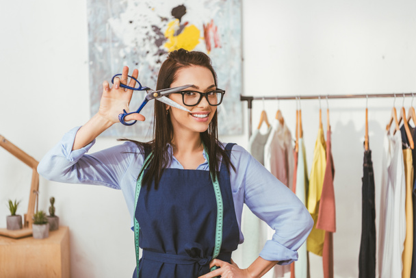 costurera sonriente posando con tijeras en el lugar de trabajo
  - Foto, Imagen
