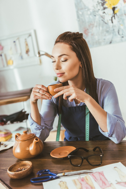 όμορφη μοδίστρα, κάθεται στο τραπέζι και πίνοντας τσάι - Φωτογραφία, εικόνα