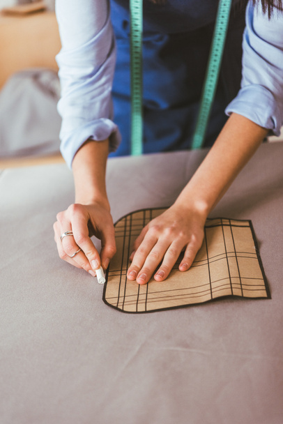 cropped image of beautiful seamstress making pattern with piece of chalk on fabric  - Photo, Image