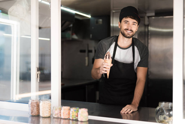 A man in an apron posing in a mobile diner. He is holding a delicious chocolate ice cream - Foto, Imagen