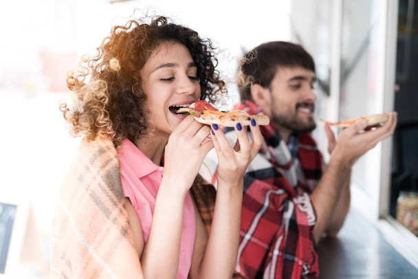 通りでモバイル スナック バーで若いカップルが立っています。彼らはおいしいピザの 2 つを注文し、それを食べる - 写真・画像